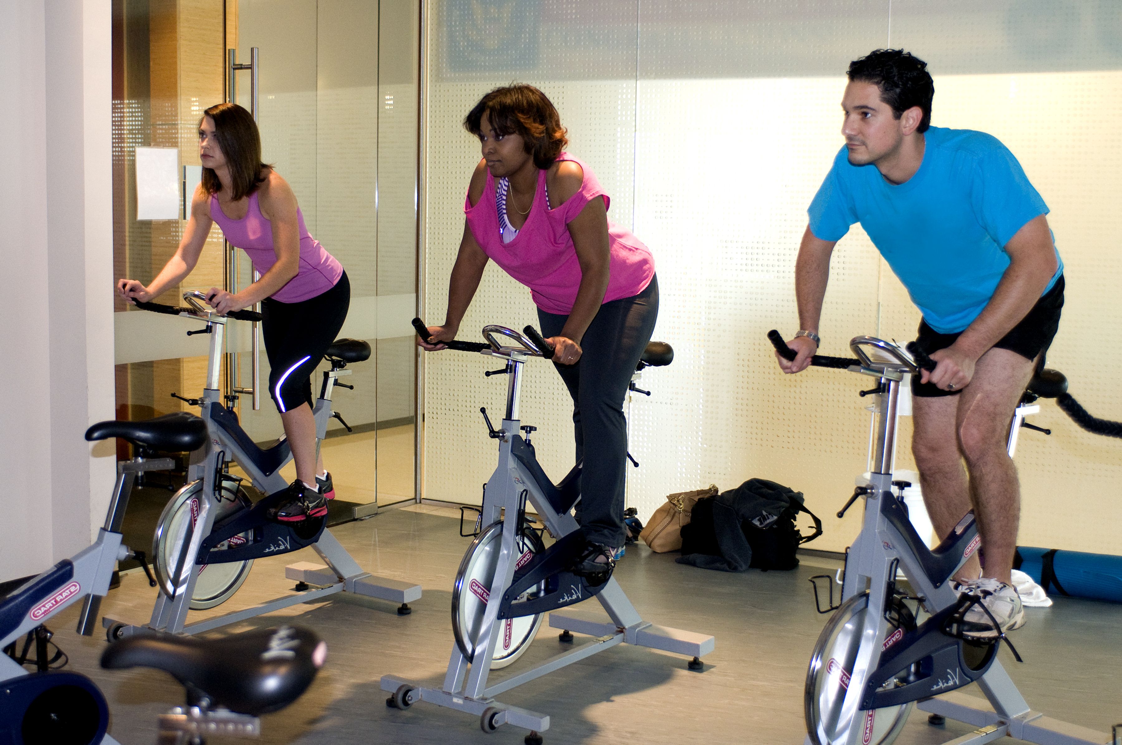 Três pessoas pedalando em bicicletas estacionárias em uma sala de exercícios.