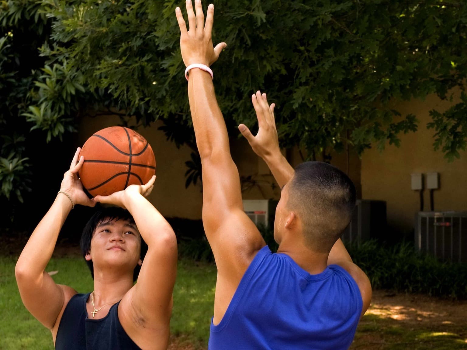 Dois jovens jogam basquete em uma quadra ao ar livre.